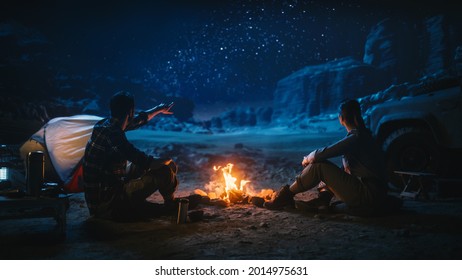 Lovely Young Couple Sitting By Campfire Watching Night Sky While Camping In The Canyon. Girlfriend And Boyfriend Tell Inspirational Nature Loving Stories About Life, Look At Milky Way Stars