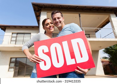 Lovely Young Couple With Sold Sign In Front Of Their Old House