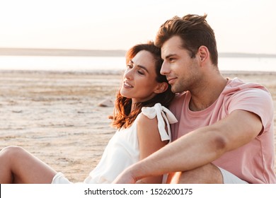 Lovely young couple wearing summer clothing relaxing on a blanket at the beach, hugging