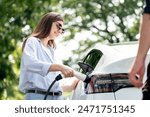 Lovely young couple wearing sun glasses recharging battery for electric car during road trip travel EV car in natural forest or national park. Eco friendly travel during vacation and holiday. Exalt