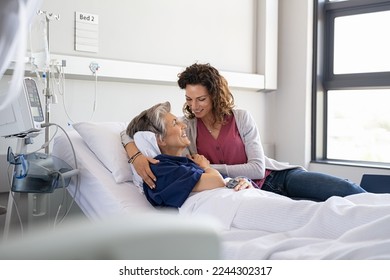 Lovely young daughter visiting old sick mother hospitalized in private clinic. Reassuring woman assisting her senior ill mother lying on hospital bed and talking. Senior and parent care concept. - Powered by Shutterstock