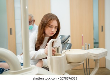 Lovely young girl children hold glass of water on one side of dental chair equipment and senior dentist as background.