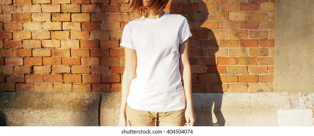 Lovely young girl wearing in a white blank t-shirt  posing against a background of a brick wall in the rays of the setting sun