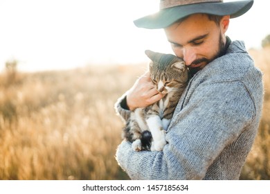 Lovely young hipster with a cat. A guy with a mustache and a beautiful smile is hugging a cat. Beautiful autumn sunset