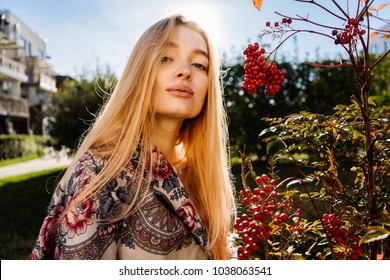 lovely young long-haired blond girl with a handkerchief on her shoulders walking around the garden in the sun, admiring the nature