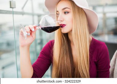 Lovely young woman drinking red wine sitting in a cafe with a great view of the city,hat,trendy outfit girl,nail art,make-up stylist,gold rings