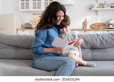 Lovely Young Woman Getting Present From Kid: Happy Mom Enjoy Reading Handmade Greeting Card From Small Son Cheerful Embrace Little Child On Mother Day, Valentine Or Birthday. Love And Care In Family