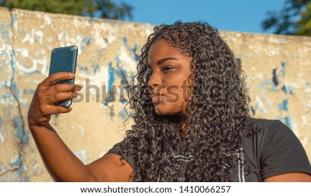 Lovely young woman with long curly hair posing for selfie, by social network post. Candid outdoor caption. Connected world and inclusive beauty concepts