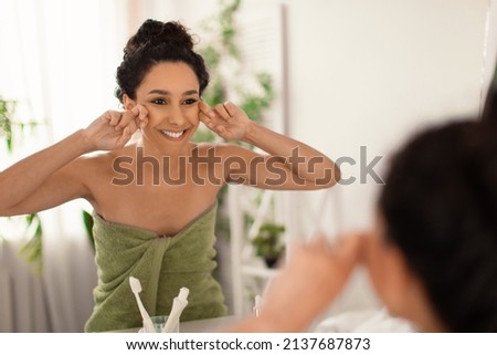 Lovely young woman making lymphatic drainage facial self massage near mirror at home, free space. Beautiful millennial female doing domestic skin care treatmenrt at bathroom