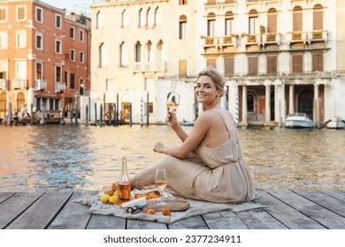 Lovely young woman picturesque picnic on the wooden gondola dock  with rose wine, fruits and snack on wooden pier in the Venice, Italy - Powered by Shutterstock