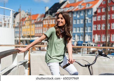 Lovely young woman posing with bike at the Nyhavn harbor pier in european city Copenhagen, Denmark, on sunny day. Visiting Scandinavia, famous European place.