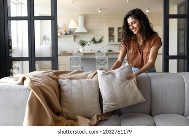 Lovely young woman putting soft pillows and plaid on comfy sofa, making her home cozy and warm, copy space. Millennial lady decorating her couch with cushions and blanket for autumn or winter - Shutterstock ID 2032761179