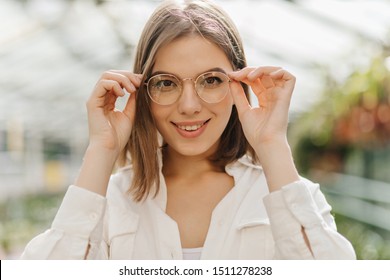 Lovely Young Woman Touching Glasses. Winsome Female Model Posing On Blur Nature Background.