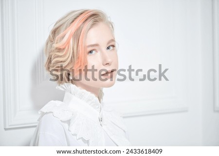 Lovely youth style. A cute teenage girl with a short haircut and blonde hair with orange streaks poses in a white blouse with a lace frill in a classic white interior. Beauty, style and fashion.