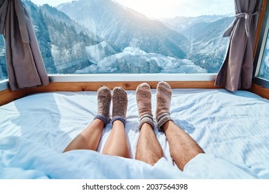 Lover couple in knitted warm socks lying on a soft cozy bedroom with snowy mountains view in a winter time 