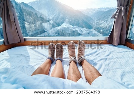 Lover couple in knitted warm socks lying on a soft cozy bedroom with snowy mountains view in a winter time 