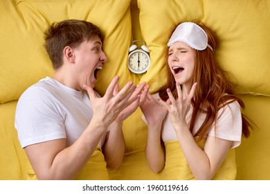 Lovers In Bed Looking Terrified As Hearing Alarm Clocks. Horrified Young Married Couple Overslept Work