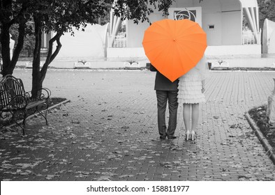 Lovers Couple On A Black And White Photo Of An Orange Umbrella. Rear View.