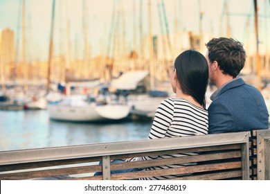 Lovers couple Romantic dating sitting on bench on date in old harbour, Port Vell, Barcelona, Catalonia, Spain. Happy woman and man embracing enjoying life and romance outside
