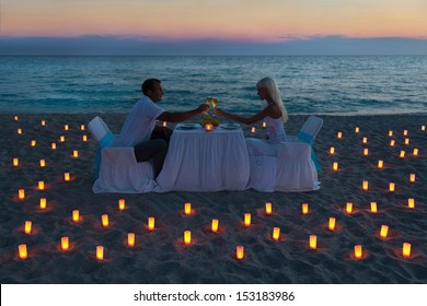 Lovers Couple Share A Romantic Dinner With Candles On Sandy Sea Beach During Sunset