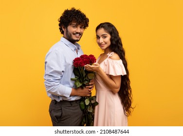 Lovers holiday. Romantic indian couple holding bouquet of flowers and looking at camera on yellow studio background. Loving guy pampering his girlfriend with roses on Valentine's Day - Powered by Shutterstock