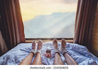 Lovers Legs In Warm Knitted Socks Lying On Soft White Comfortable Bed At Window With Idyllic Calm Serene View 