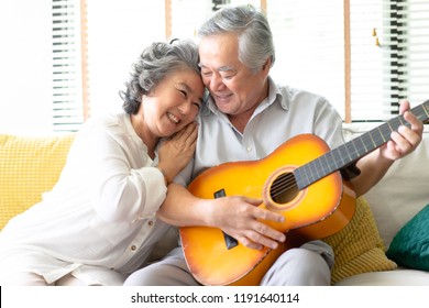 Lovers in a living room.Happy senior woman hugging bearded man in love sitting on the sofa while young husband playing guitar in living room. - Powered by Shutterstock