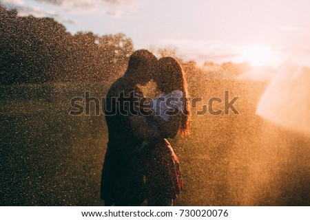 Lovers in the rain. The guy hugs the girl. Raindrops against the sunset background.