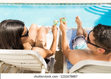 Lovers toasting champagne while relaxing on comfortable chairs at poolside in vacation - Powered by Shutterstock