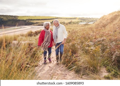 Loving Active Senior Couple Walking Arm In Arm Through Sand Dunes On Winter Beach Vacation - Powered by Shutterstock