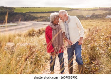 Loving Active Senior Couple Walking Arm In Arm Through Sand Dunes On Winter Beach Vacation