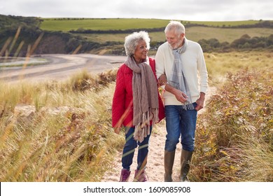 Loving Active Senior Couple Walking Arm In Arm Through Sand Dunes On Winter Beach Vacation - Powered by Shutterstock