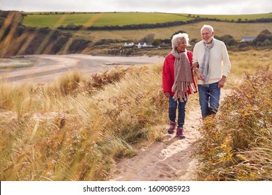 Loving Active Senior Couple Walking Arm In Arm Through Sand Dunes On Winter Beach Vacation - Powered by Shutterstock