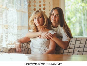 Loving Adult 20s Daughter Hug Elderly Mother From Behind While Mom Sitting On Couch People Posing Looking At Camera Smiling Feels Happy, Concept Of Multi Generational Family, Relative Devoted Person