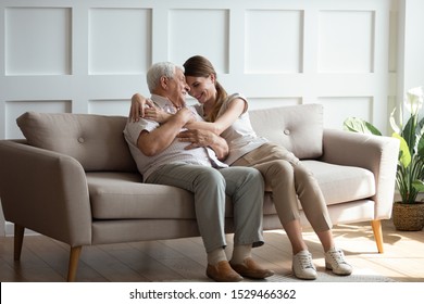 Loving adult grown up granddaughter hug old grandfather sitting on sofa in sunny living room, different generations woman and man relative people understanding connection care sincere feelings concept