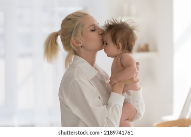 Loving affectionate mother kisses newborn baby in diaper, standing in warm cozy domestic room, enjoy happy motherhood, express caress, feeling love to infant child at home. Maternity, babyhood - Shutterstock ID 2189741761
