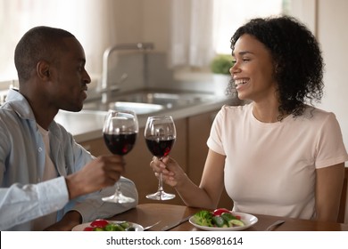 Loving African American Couple Sit At Table Having Dinner Drink Wine Celebrating Marriage Anniversary, Smiling Happy Biracial Husband And Wife Enjoy Romantic Date At Home, Eat Healthy Vegetarian Food