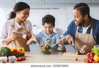 A loving African American family enjoys quality time in their kitchen. Parents and their son prepare a healthy salad, sharing smiles and laughter while bonding over fresh ingredients. - Powered by Shutterstock