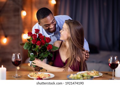 Loving African American Guy Surprising His Beautiful Girlfriend With Roses Bouquet, Greeting With International Women's Day, Happy Multicultural Couple Celebrating Holiday On Date In Restaurant