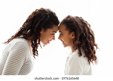 Loving African American Mom And Daughter Touching Each Other With Foreheads Over White Background, Side View. Happy Black Young Woman And School Girl Mother And Child Bonding Over White