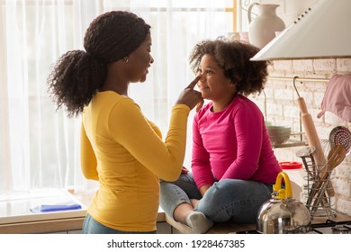 Loving African American Mother And Cute Little Daughter Having Fun And Bonding Together In Kitchen, Young Black Mom Playfully Touching Nose Of Her Female Kid, Child Sitting At Table, Side View