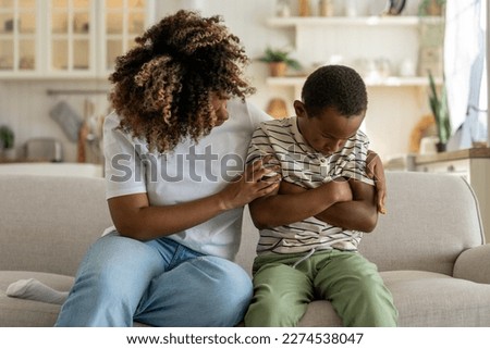 Loving african american mother embracing hugging sad little son supporting child, mom parent trying to make peace with offended upset kid, sitting together on sofa at home. Parent-child conflict