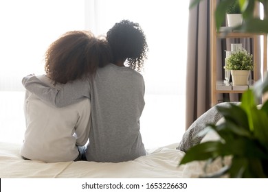 Loving African American Single Mother Sister Embrace Teen Daughter Sit On Bed Looking At Window, Parent Mom Hug Support Protect Teenage Girl, Family Trust Hope Talk Understanding Concept, Rear View
