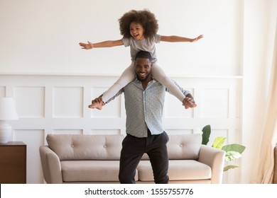Loving african American young dad carry preschooler mixed race daughter on shoulder play at home together, happy biracial father and girl child have fun entertain in living room on weekend - Powered by Shutterstock