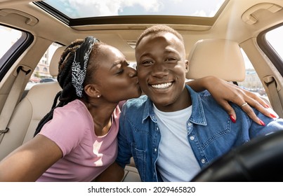 Loving afro american couple taking selfie while having car trip, sitting in auto, hugging and cheerfully smiling at camera, pretty millennial black lady kissing her boyfriend, closeup portrait