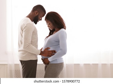 Loving Afro Man Holding His Wife Belly Over Big Window, Parenthood Concept, Copy Space