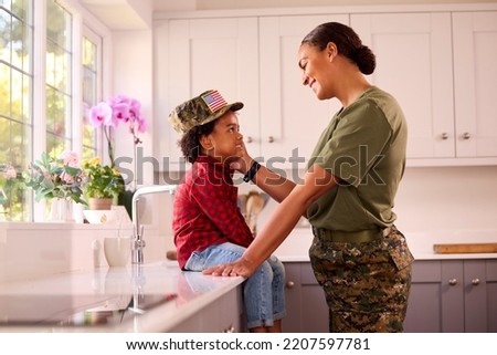 Loving American Army Mother In Uniform Home On Leave With Son Wearing Her Cap In Family Kitchen