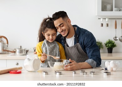 Loving Arab Father Teaching His Little Daughter How To Make Dough While They Baking In Kitchen, Happy Middle Eastern Dad And Cute Female Child Wearing Aprons, Enjoying Cooking Together, Closeup