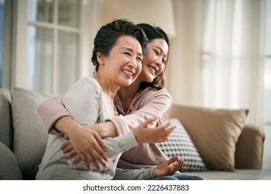 loving asian adult daughter sitting on couch at home hugging senior mother happy and smiling - Powered by Shutterstock