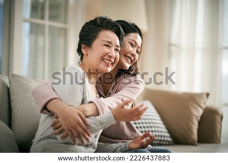 loving asian adult daughter sitting on couch at home hugging senior mother happy and smiling